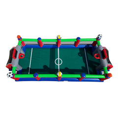 A colorful inflatable foosball game with soccer balls and a green playing field, suitable for outdoor events.